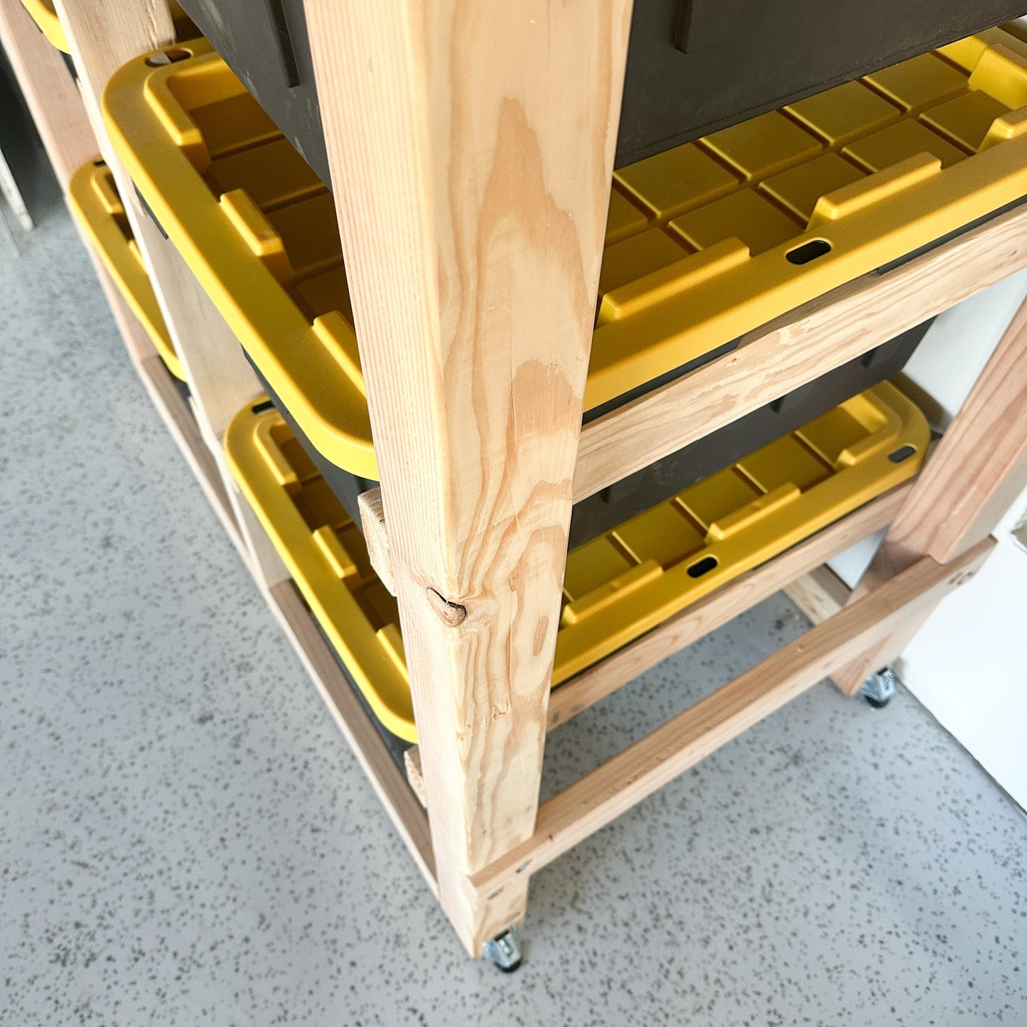 Wooden rolling cart with yellow plastic bins on a concrete floor.