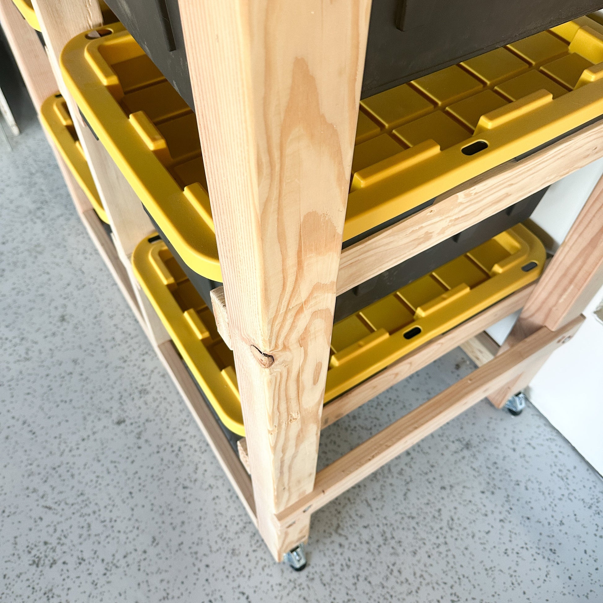 Wooden rolling cart with yellow plastic bins on a concrete floor.