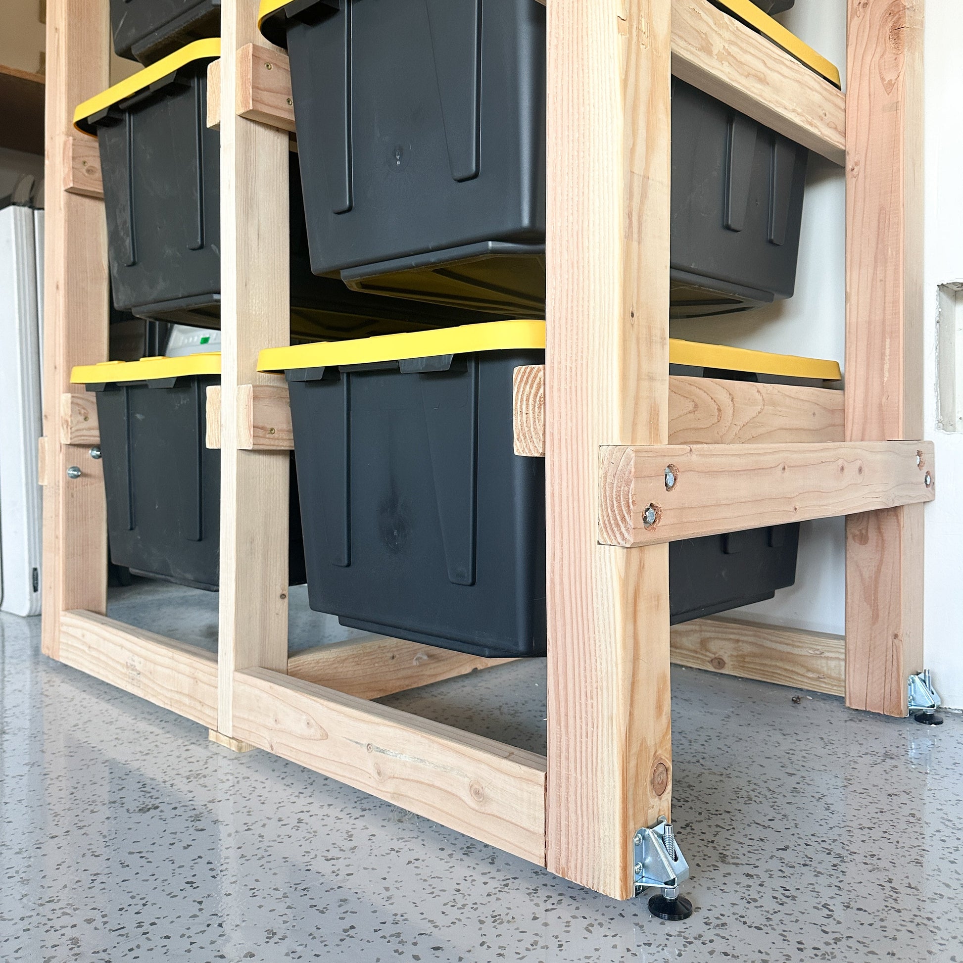 Stack of black storage bins on a wooden pallet with yellow straps.