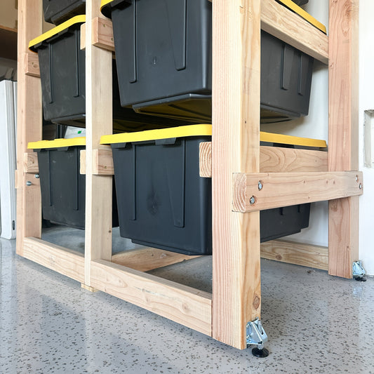 Stack of black storage bins on a wooden pallet with yellow straps.